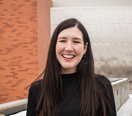 Annika Johnson, a sixth-year graduate student in the department of history of art and architecture, smiles and stands in front of a brick and white stone building